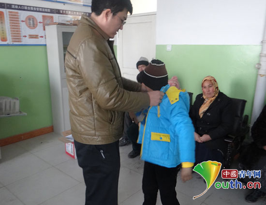 麦盖提县团委组织志愿者为贫困儿童发温暖包,图为县团委干部在为孩子穿棉衣。